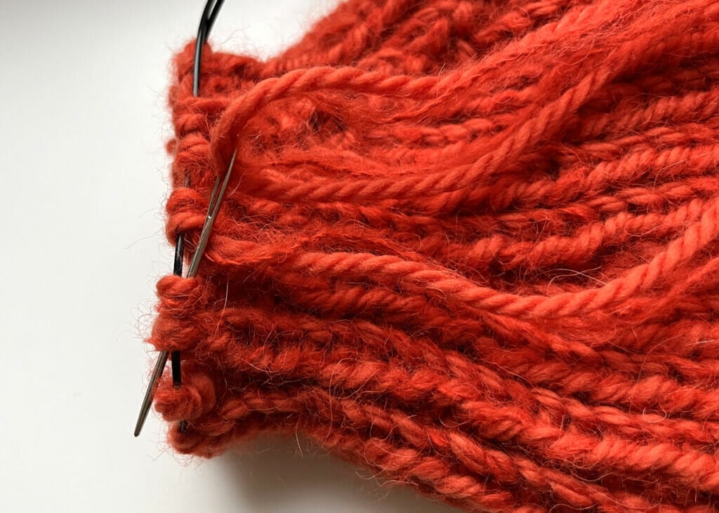Die Fäden der gestrickten Mütze werden zum Schluss mit Wollnadeln kreisförmig vernäht.