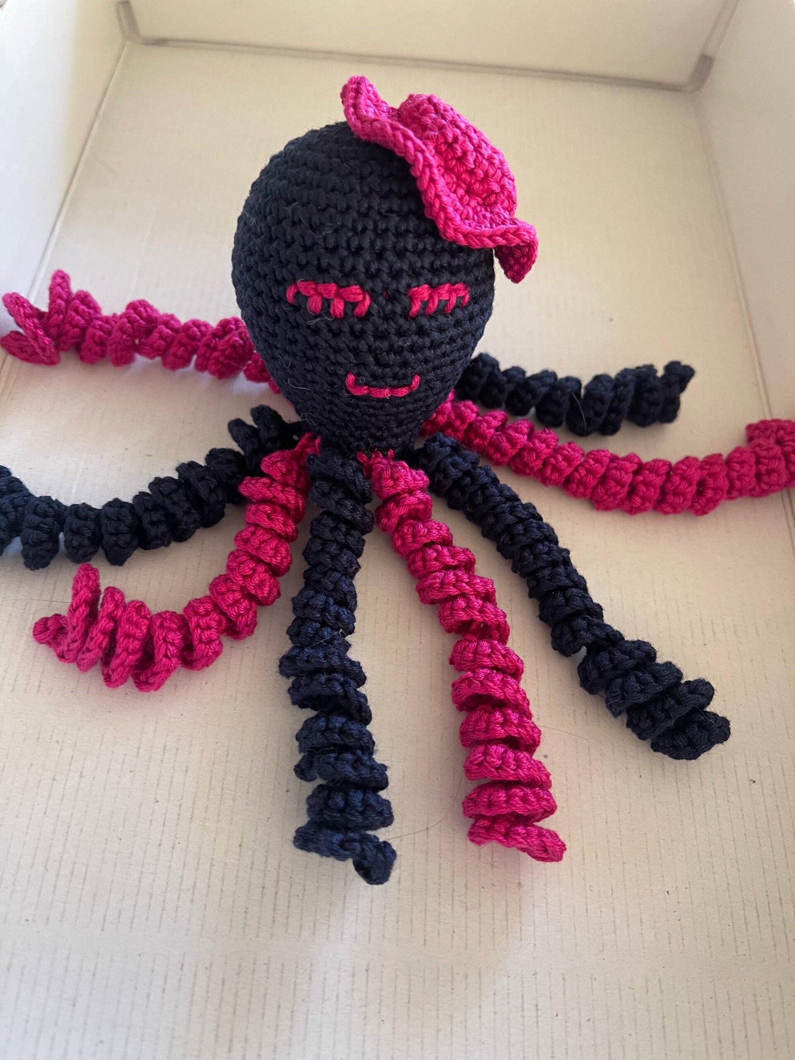 Ein dunkelblauer Häkeloktopus mit pinken Armen und einer pinken Blume, Archiv 2023.