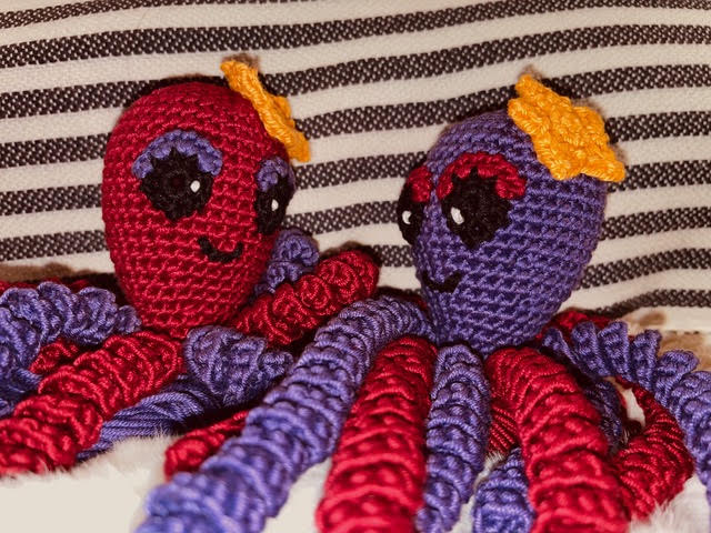 Ein roter und ein violetter gehäkelter Oktopus auf gestreiftem Stoff, Archiv 2023.