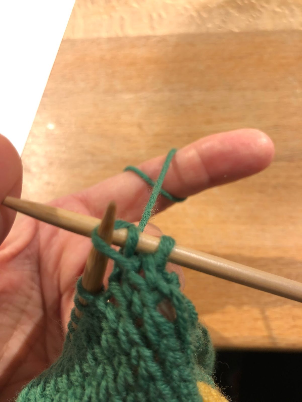 Eine Hand strickt mit grünem Garn auf einer Holznadel.