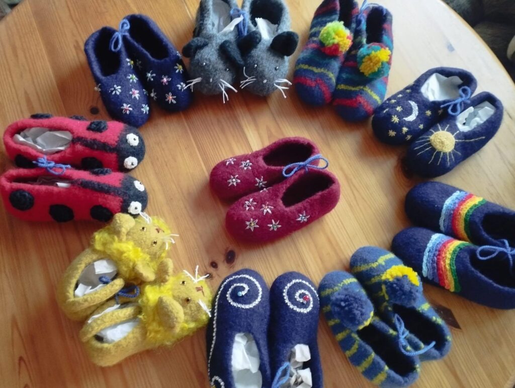 Viele bunte gestrickte und gefilzte Kinderfinken liegen im Kreis auf einem Holztisch.