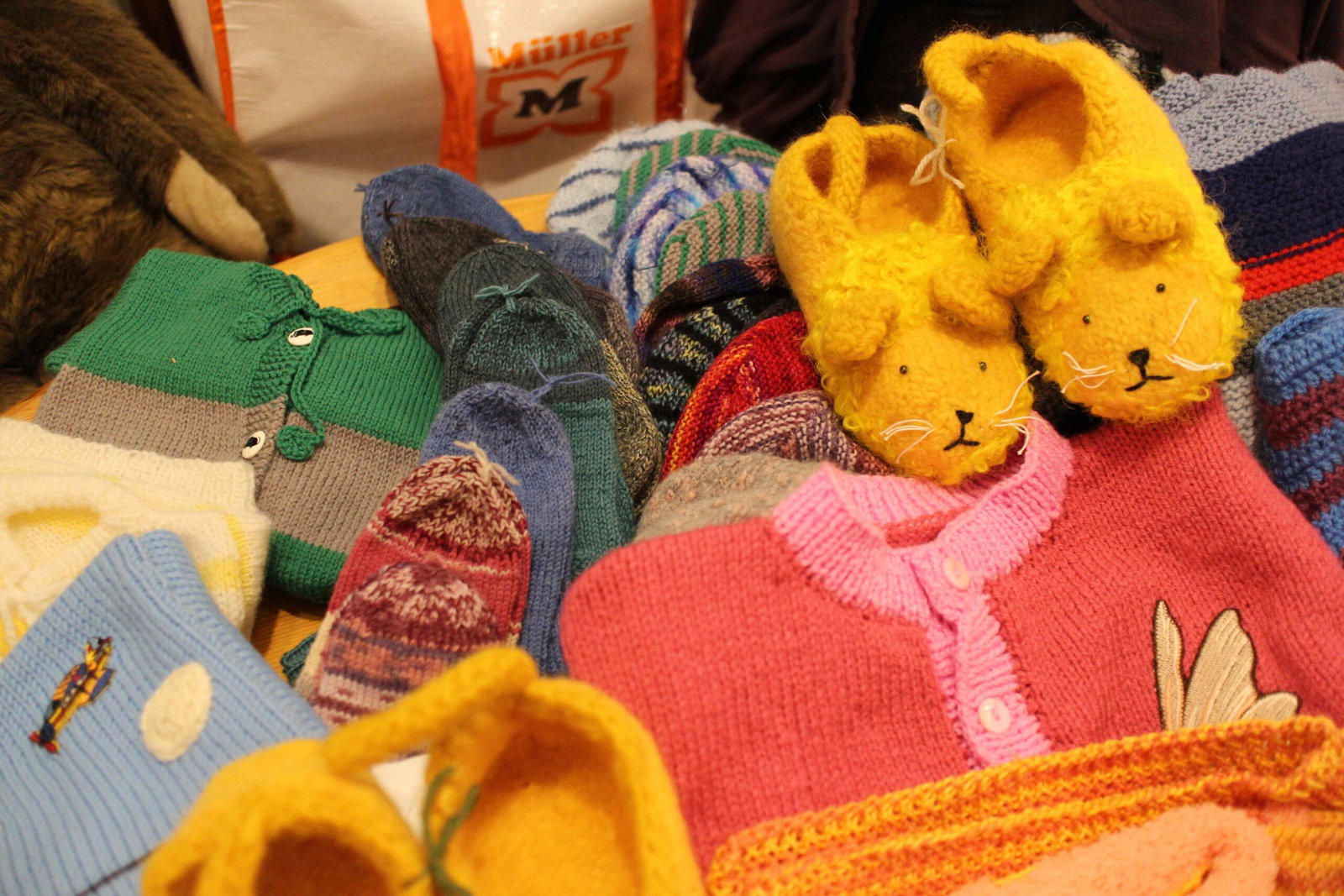 Bunte gestrickte Kinderkleidung und gelbe Finken auf einem Tisch, Archiv Juli 2024.